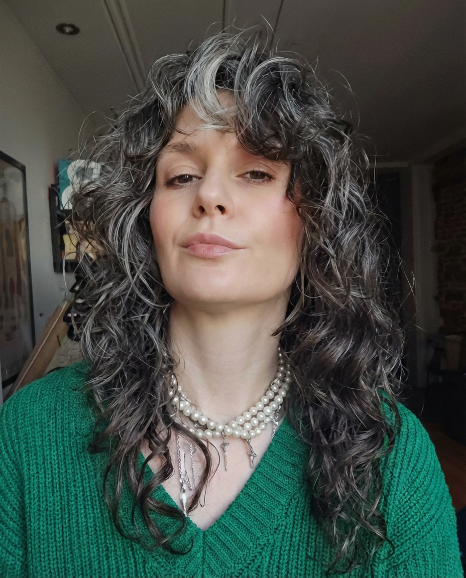 Studio close-up of woman with silver-highlight curly shag layers, curtain fringe, and natural texture generated by blondefilter.net