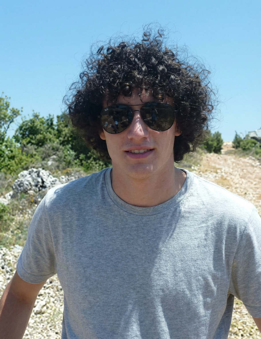 Outdoor candid of man wearing sunglasses with wind-tousled Jewfro curls against blue sky generated by blondefilter.net