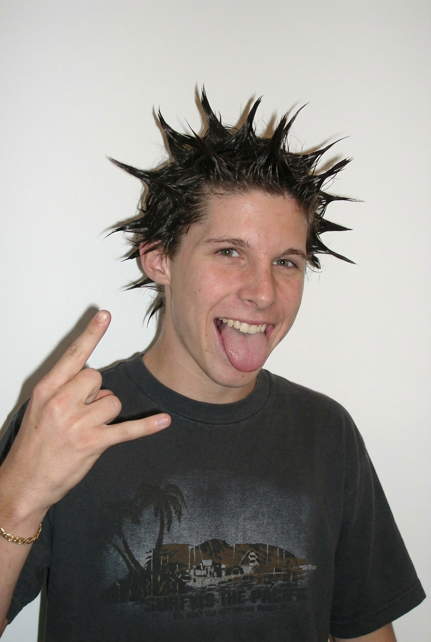 Smiling teen giving rock hand sign while wearing short dark liberty spikes against a white wall generated by blondefilter.net