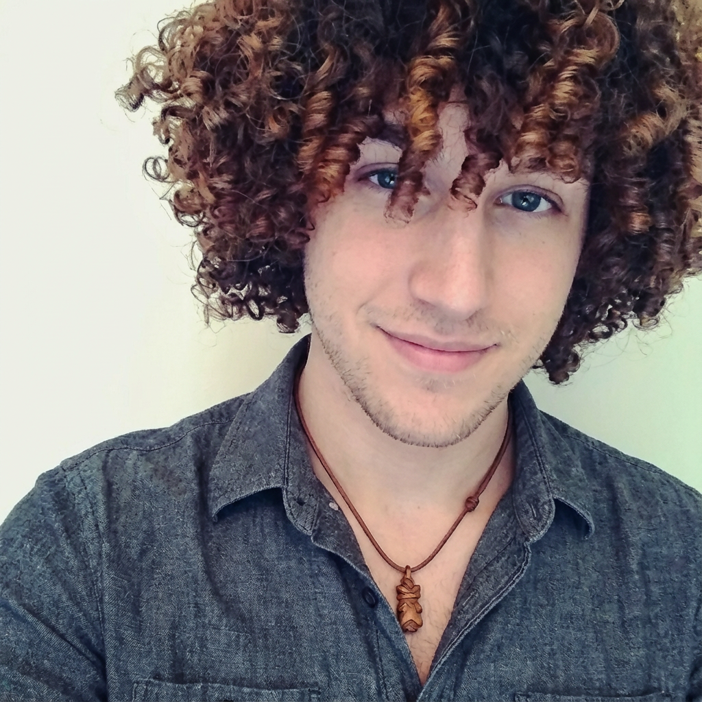 Smiling man with medium-length tight corkscrew curls wearing a grey chambray shirt against a light background, generated by blondefilter.net