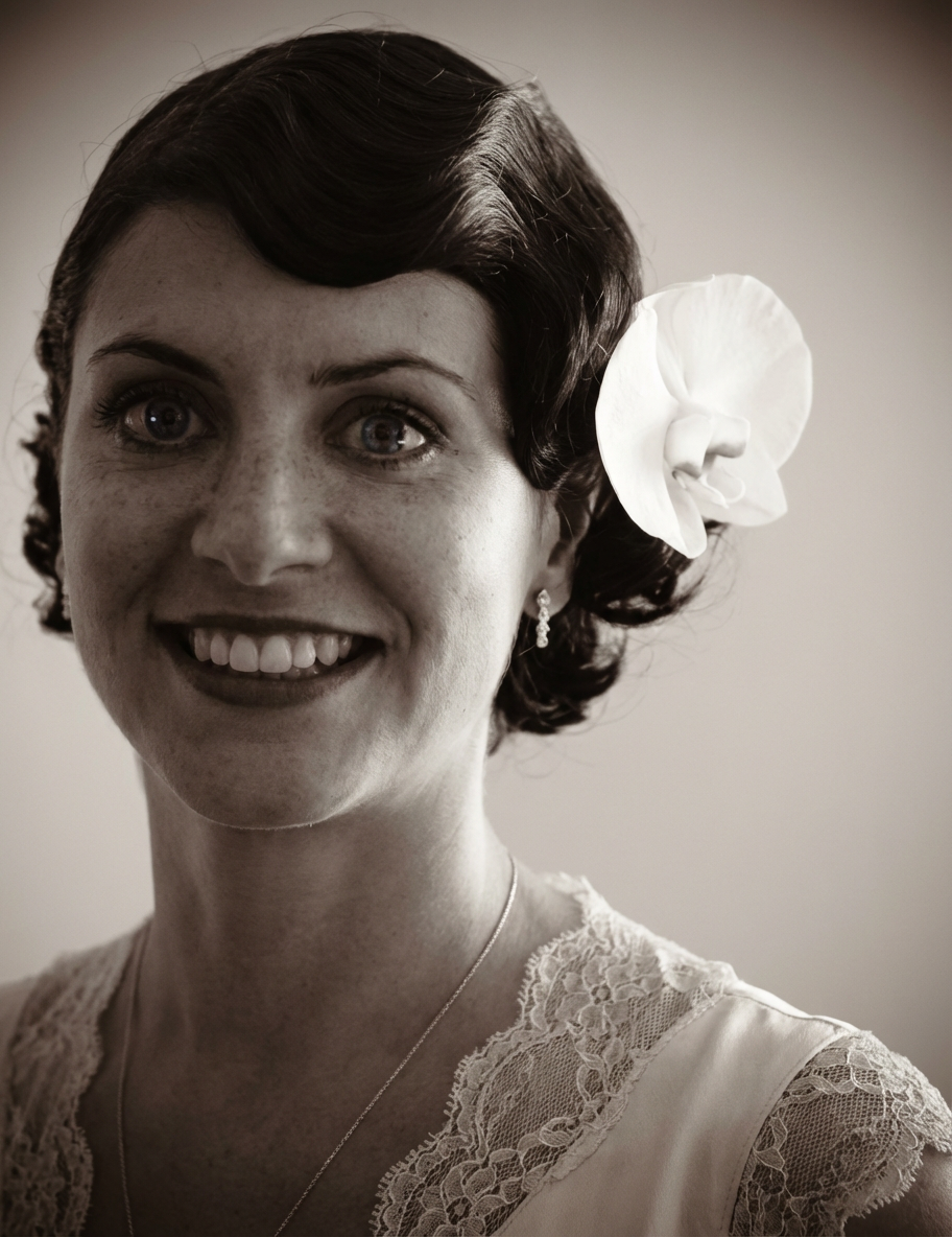 Smiling woman with polished Marcel waves and a large flower accessory tucked above her ear in gentle natural light, generated by blondefilter.net