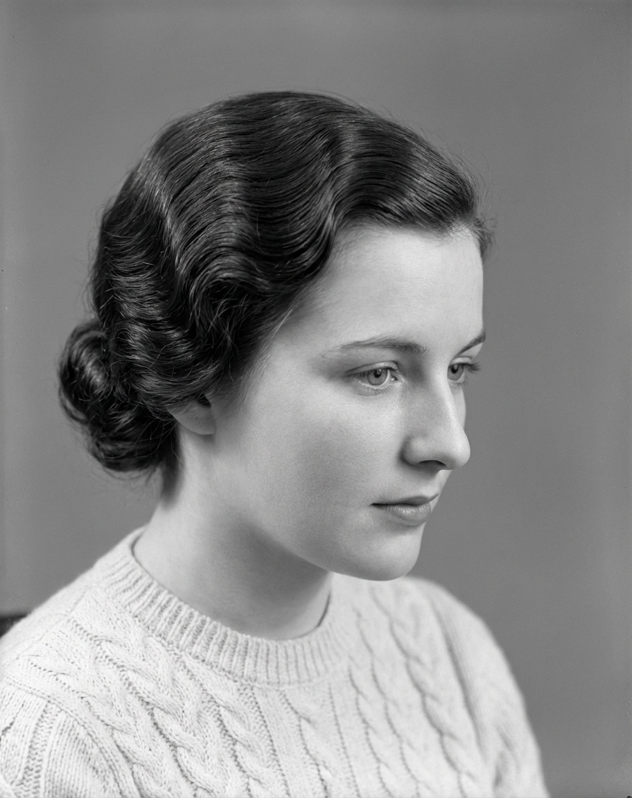 Side profile of woman wearing smooth Marcel waves swept back into a low chignon against a clean studio backdrop, generated by blondefilter.net