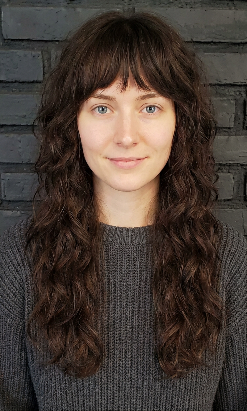 Studio portrait of woman with long dark wavy shag and full fringe against a brick wall generated by blondefilter.net