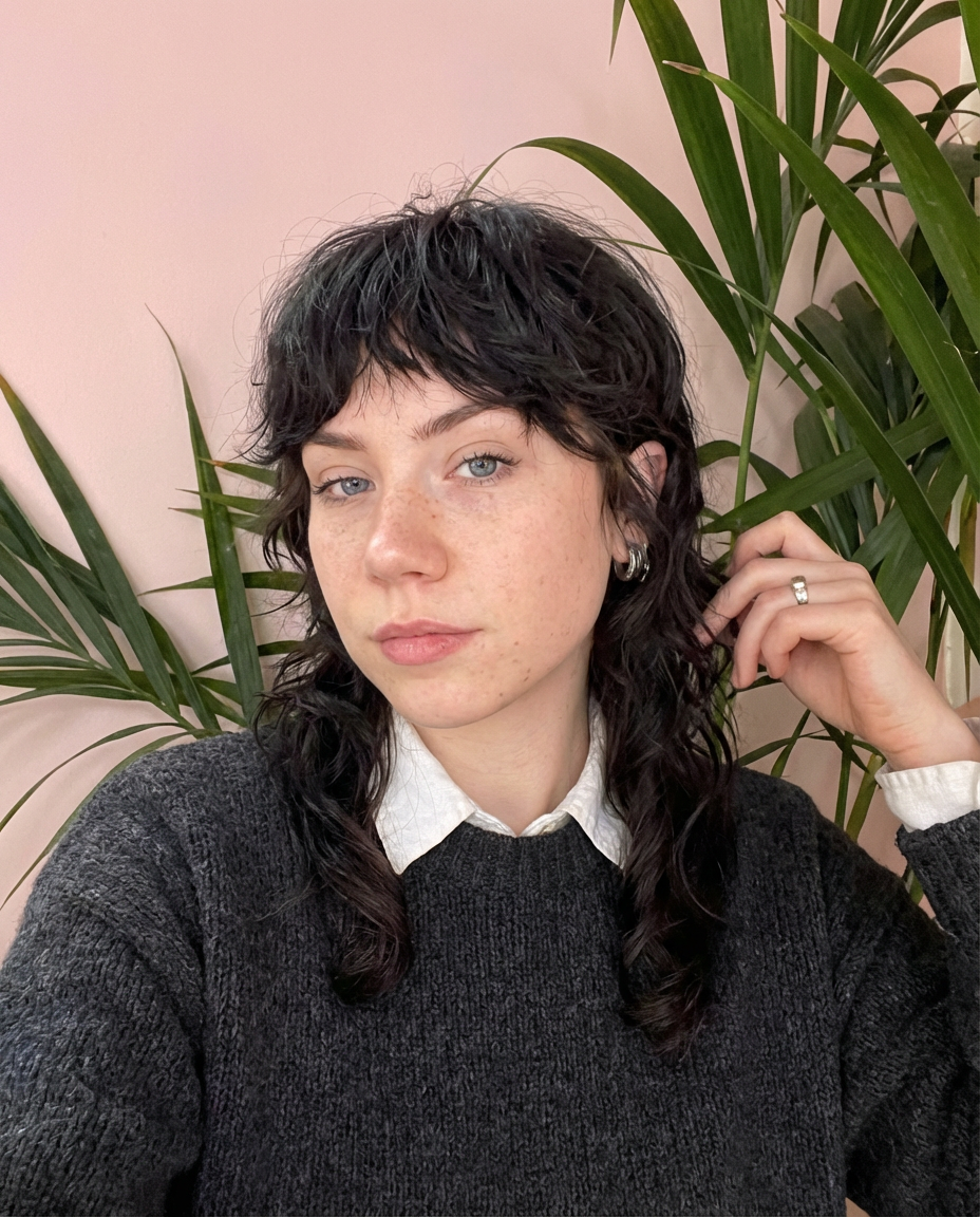 Selfie of woman with choppy black wavy shag mullet and curtain bangs in front of pink wall and plants generated by blondefilter.net